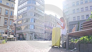 Tired blond fashion woman traveler sitting on bench and waiting for bus. Resting after a long journey.