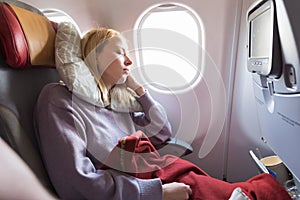 Tired blonde casual caucasian lady sleepin on seat while traveling by airplane. Commercial transportation by planes.