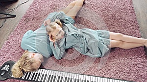 Tired blonde girls relax at home on a pink carpet. Near electronic piano.