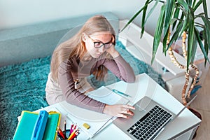 Tired and boared beautiful young school girl left-handed working at home in her room with a laptop and class notes studying in a