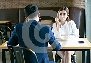 Tired bored Asian girl sitting and lunch with her boyfriend at a cafe and looking away.Young emotional couple get quarreled in