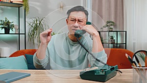 Tired bored Asian man talking on wired telephone exhausted of talk, making silly faces, fooling