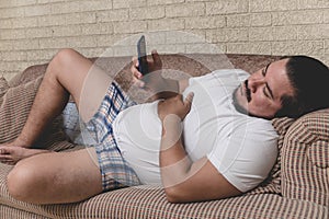 A tired and bored slacker in boxer shorts is addicted on the phone during a lazy day lying on the couch photo