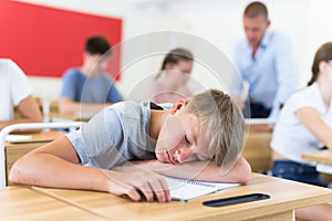 Tired bored teenage schoolboy sleeping at desk