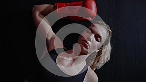 Tired boxer woman is lying down after hard training in boxing gym, wearing sport clothes and red boxing gloves. Female