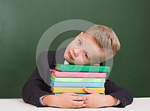 Tired boy lying on books in classroom