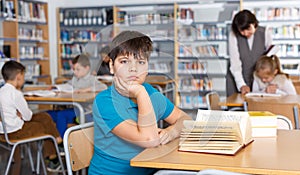 Tired boy reading textbooks in school library