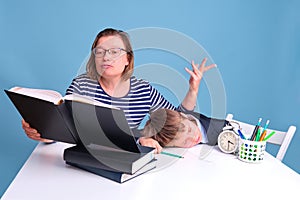 Tired boy schoolboy sleeping at a school desk and mom doing homework, blue background