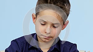 Tired boy sitting at a table and yawns. Blue background