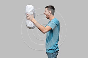 Tired brunet man in a blue tee holding white pillow isolated over grey background.