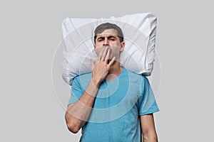 Tired brunet man in a blue tee resting on a white pillow isolated over grey background.