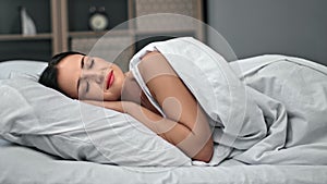 Tired brunette woman relaxing on comfortable bed with white cotton pillow and sheet blanket sleeping