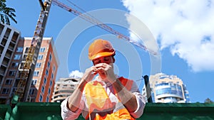 Tired builder in protective helmet sitting on the construction site outdoors. Business, building, industry concept. Slow