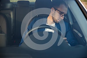 Tired business man falling asleep sitting inside her car seen through windshield