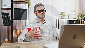 Tired business man taking break from work wearing 3D glasses earing popcorn watching film on laptop