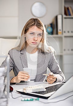 Tired business woman drinking headache pills in office