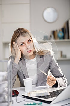 Tired business woman drinking headache pills in office