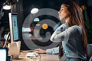 Tired business woman with neck pain looking uncomfortable while working with computer in the office at night