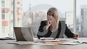 A tired business woman sits in the office and checks various documents lying on the table. A female accountant checks