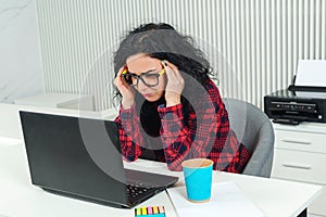 Tired business woman at workplace. Stressed woman working on laptop in modern office. Woman holding hand on head. Hard working day