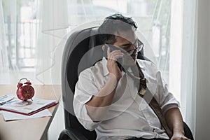 Tired businessman asian during a phone call sleeping on workplace at office desk surrounded by paperwork..