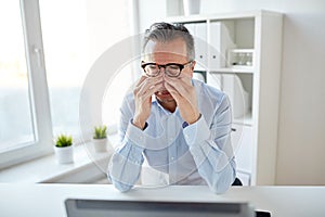 Tired businessman in glasses with laptop at office photo