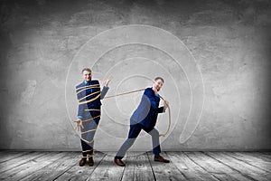 Tired businessman pulls tied himself with a rope.