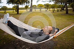 Tired businessman resting in nature on hammock in park.