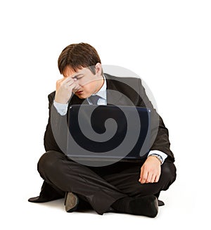 Tired businessman sitting on floor with laptop