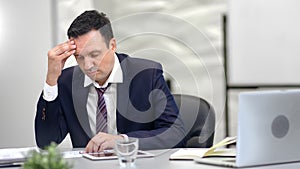 Tired businessman in suit having headache in front of laptop at office