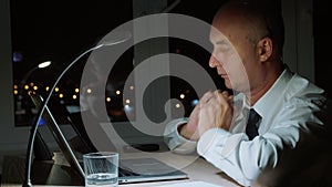 Tired businessman working by notebook and doing neck massage in night office