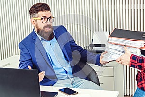 Tired businessman working with papers in office. Young bearded employee unhappy with excessive work