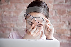 Tired businesswoman holding eyeglasses and massaging nose bridge