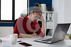 Tired businesswoman sitting at startup business desk looking at laptop screen.