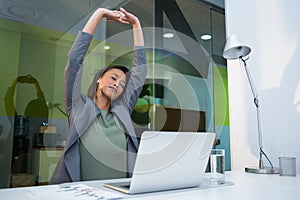 Tired businesswoman stretching her arms up at desk