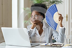 Tired businesswoman waving paper fan exhausted of heat overheated at workplace in office or at home