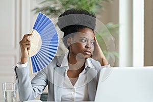 Tired businesswoman waving paper fan exhausted of heat overheated at workplace in office or at home
