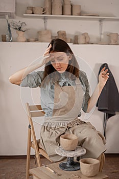 Tired caucasian beautiful female potter at workplace. creation of handmade pottery. a potter in a ceramics studio