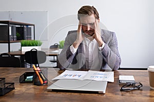 tired caucasian businessman sitting in front of documents in the office massaging his head temples