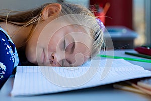 Tired caucasian schoolgirl sitting at desk and lying on books in classroom at elementary school