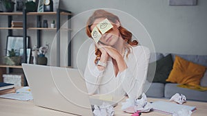 Tired Caucasian woman napping sits at table with stickers on eyes.