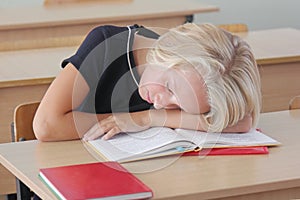 Tired child schoolgirl sleeps during a lesson at the desk in a classroom