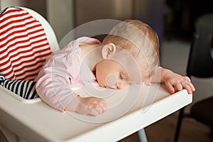 Tired child sleeping in highchair after the lunch. Cute baby girllying his face on the table tray.