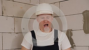 A tired construction worker in a white hard hat is standing in a new apartment.