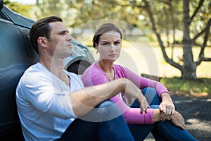 Tired couple sitting by breakdown car