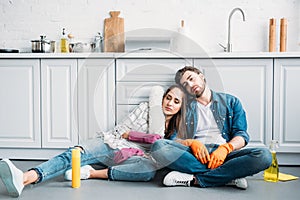 tired couple sitting on floor and leaning on kitchen counter after cleaning
