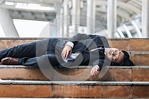 Tired depressed young Asian business man lying down on stairs and suffering from severe depression. Unemployment and layoff