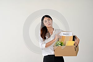 A tired and despairing Asian businesswoman holds a cardboard box with her resignation letter