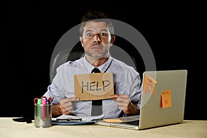 Tired desperate businessman in stress working at office computer desk holding sign asking for help