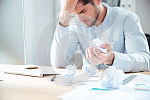 Tired desperate young businessman working and crumpling paper